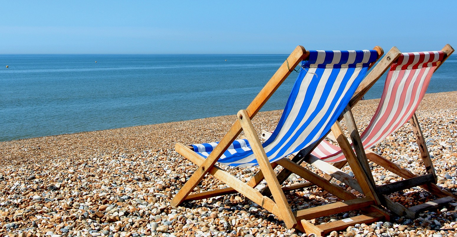 Two deckchairs on a pebbled beach, facing out to sea