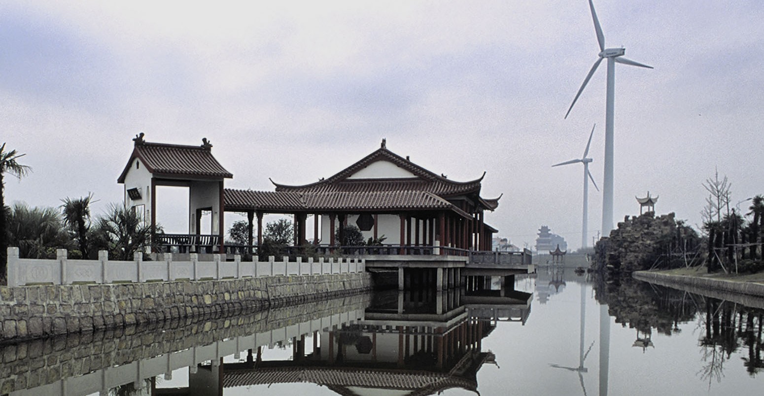 A small temple rests in the shadows of a wind turbine spinning at the Fengxian Wind Farm site in Shanghai, China.