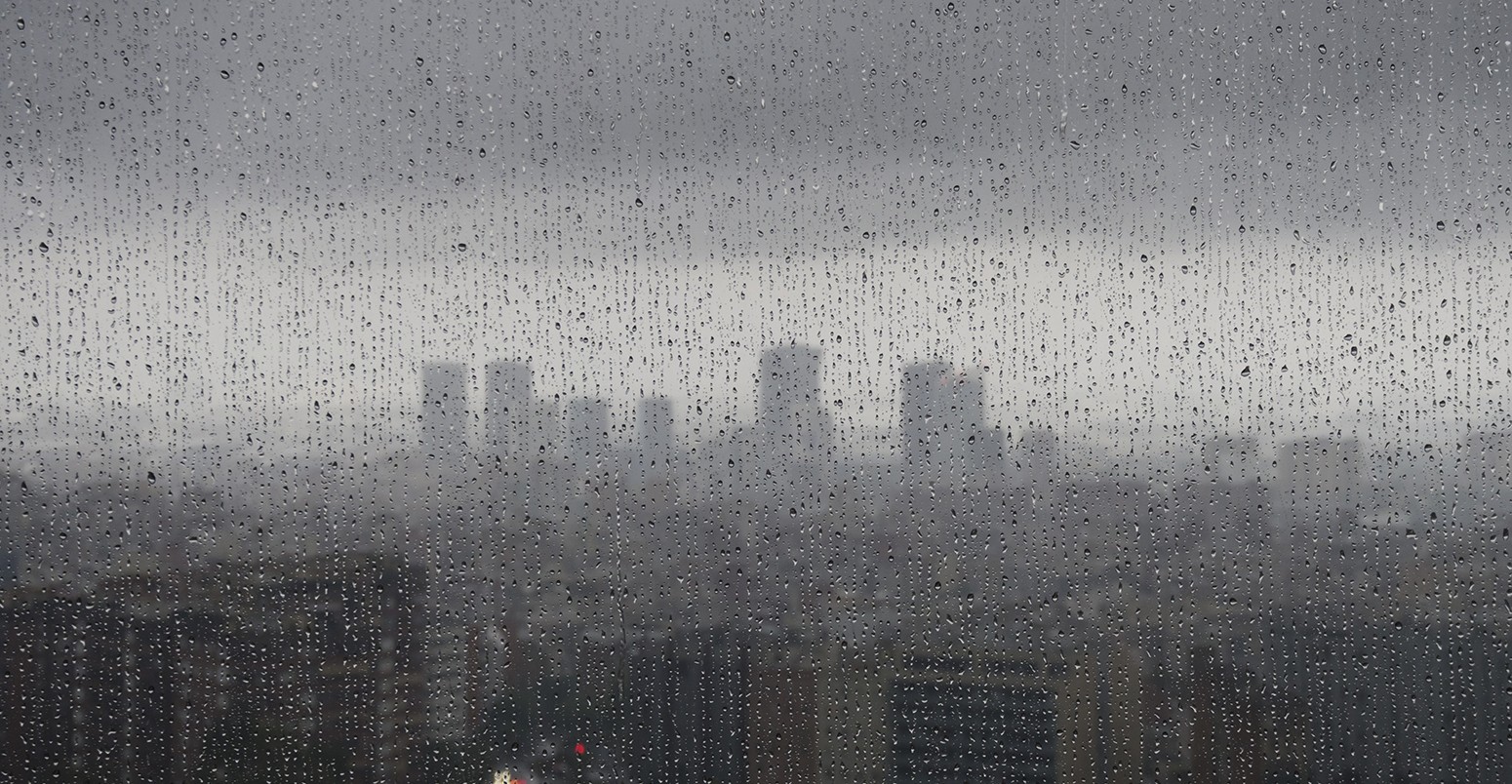 After heavy rainfall, the diffuse skyline of Barcelona is emerging in the twilight behind raindrops on a window