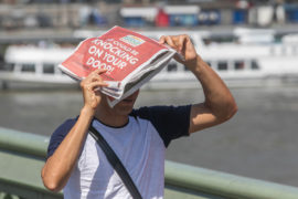 A pedestrian on Waterloo Bridge shelters with a newspaper from the sun. 25 July 2019, London.