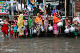 Women and children collect drinking water from a water logged area in Dhaka, Bangladesh, June 2017. Credit: Mehedi Hasan/Alamy Stock Photo.