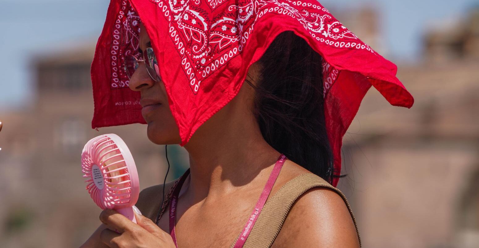 A woman with a portable fan covers her head from the soaring heat.