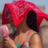 A woman with a portable fan covers her head from the soaring heat.