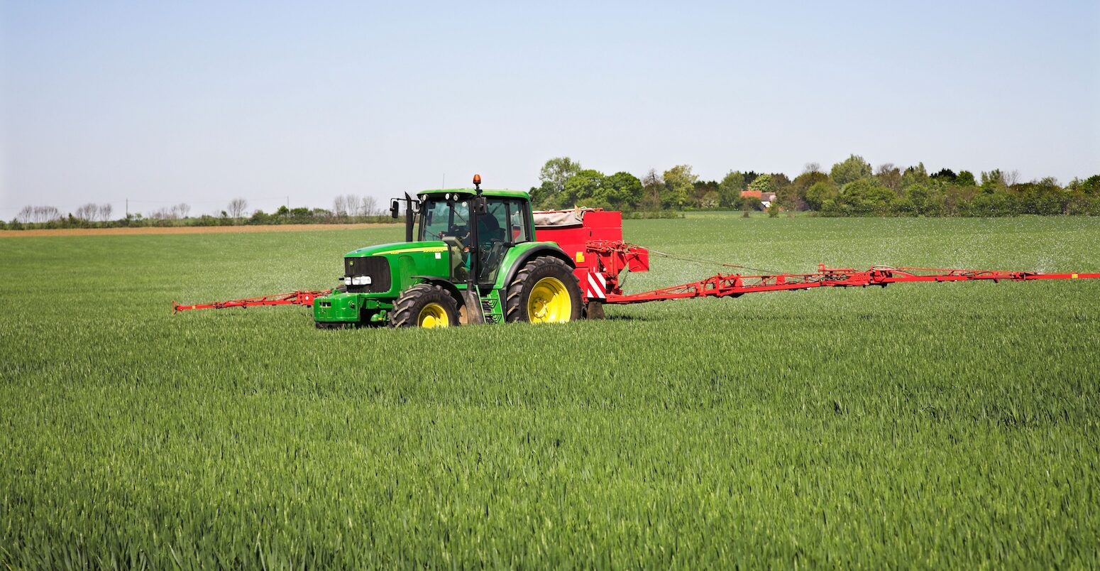 A tractor-drawn applicator applies nitrogen granule fertiliser to a field of corn.