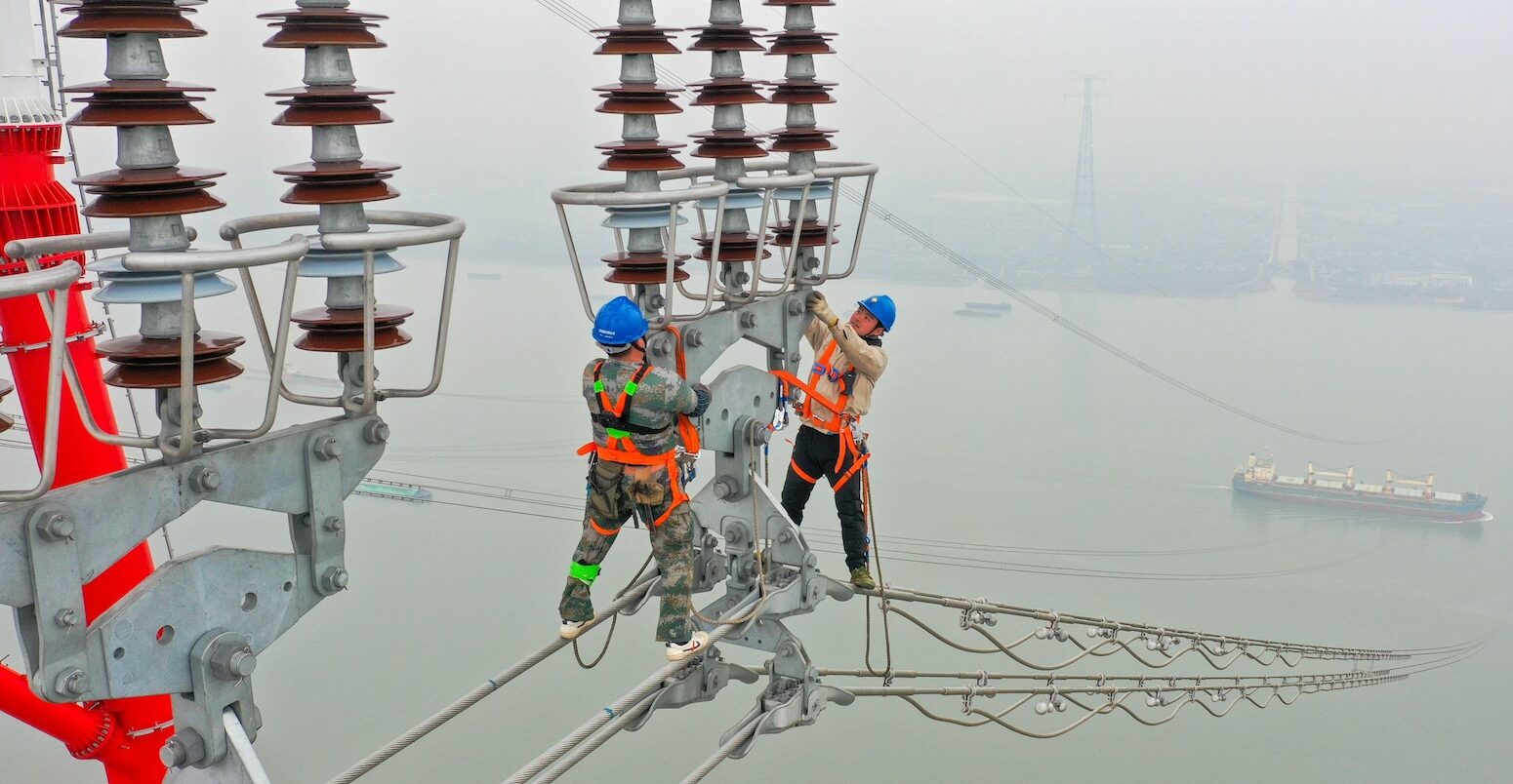 Construction workers inspect power transmission tower.