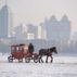 Horse and carriage crosses the frozen Songhua River with the city of Harbin in background. Heilongjiang Province, China.